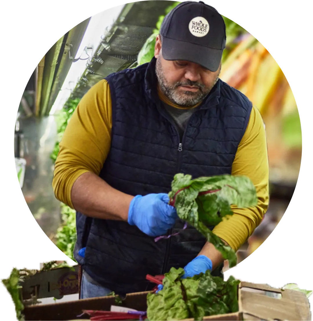 A Whole Foods Market employee wearing gloves carefully handles fresh chard