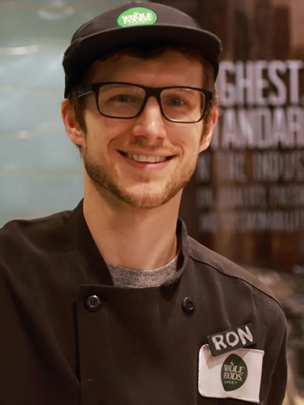 Smiling man wearing glasses and a Whole Foods hat and name tag, potentially related to dental or vision insurance services.