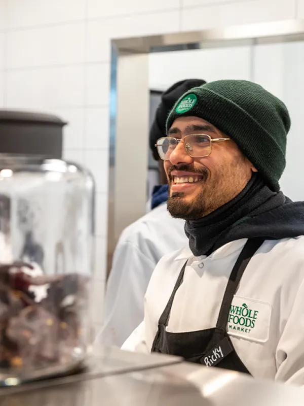 Smiling Whole Foods Market employee wearing a green beanie and apron.