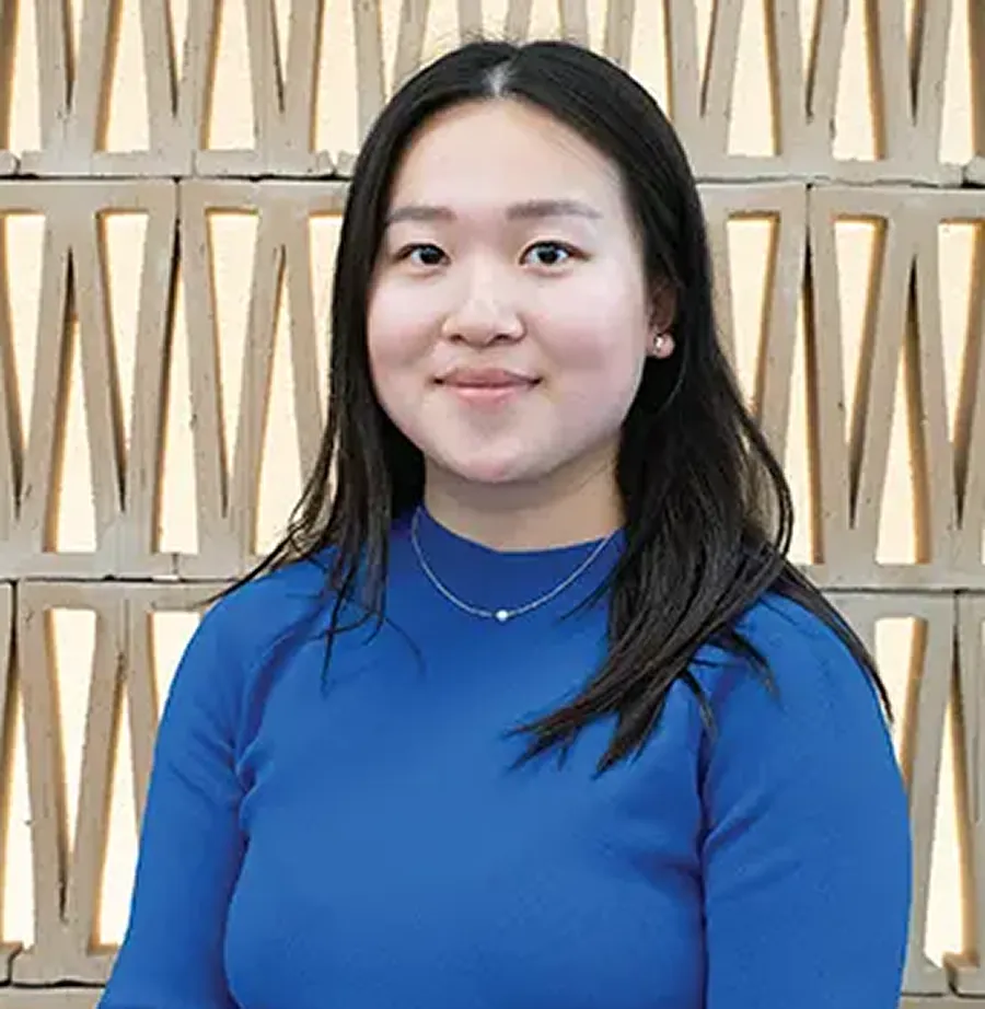 Hannah smiling, wearing a blue top, in front of a textured wall.