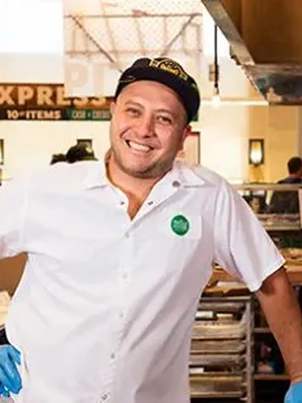 Man smiling in white uniform with Whole Foods logo, suggesting healthy food options and overall wellness.