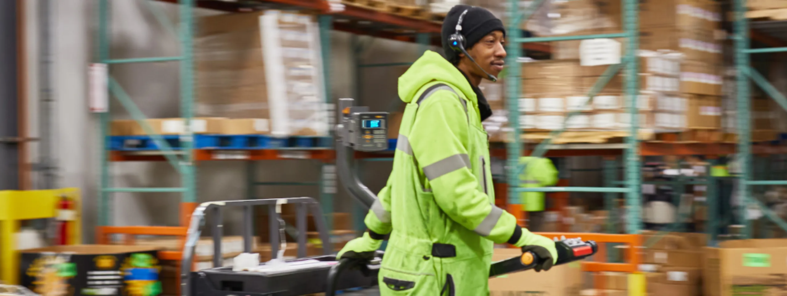 Warehouse worker operating a forklift with a headset.