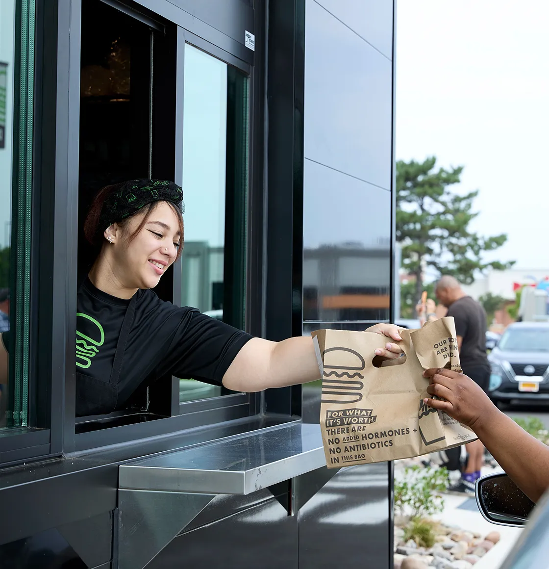 A worker hands a customer a food order at a drive-thru window