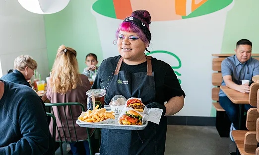 Shake Shack employee carrying a tray of food including burgers and fries