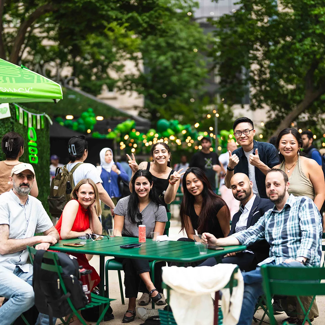 Group of smiling people sitting at a green table outdoors