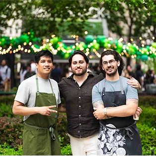 Three smiling Shake Shack employees stand together outdoors
