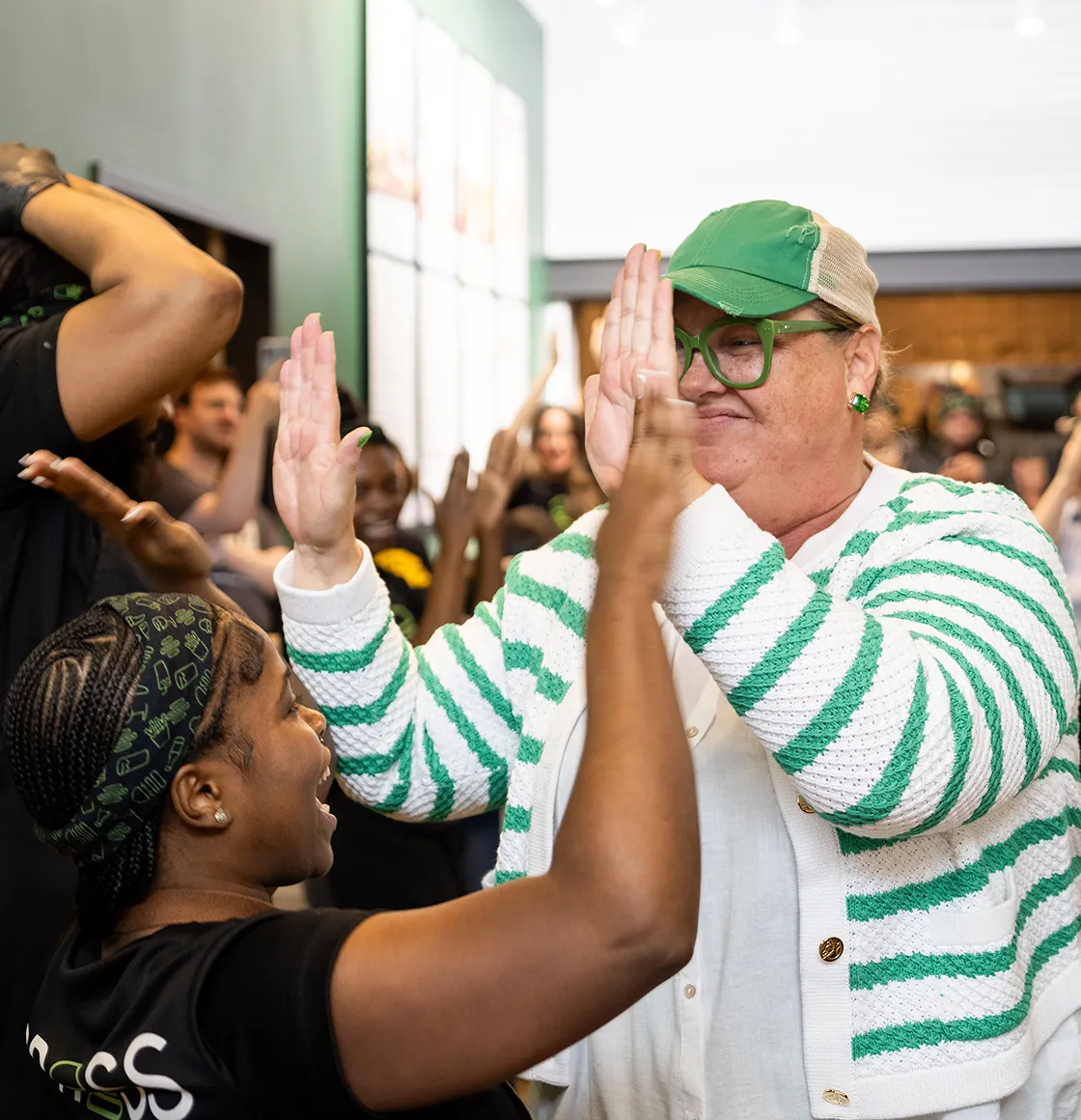 Two women give each other a high five surrounded by a group of people