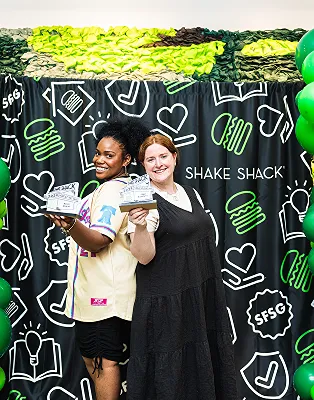 Two Shake Shack employees holding awards in front of a branded backdrop