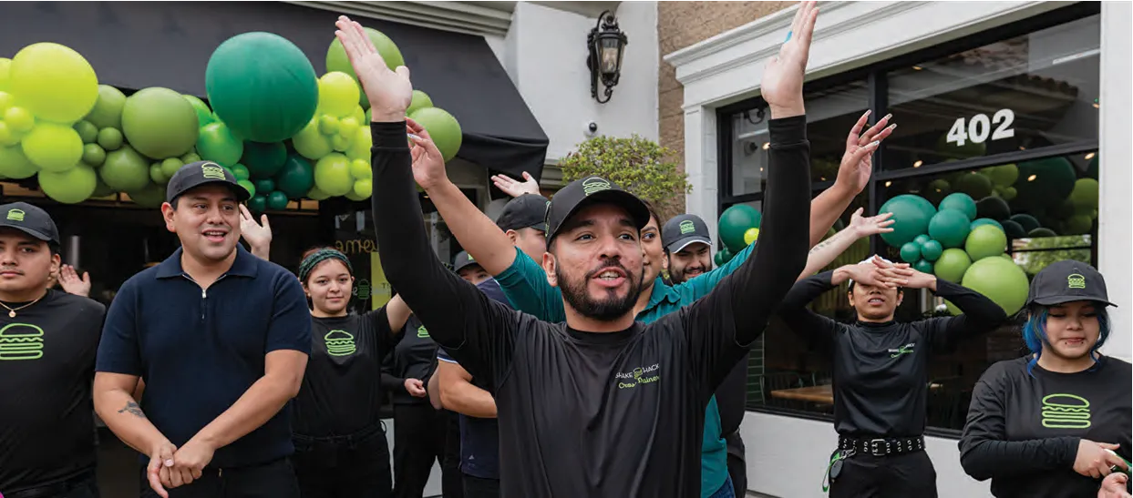 Shake Shack crew celebrating a new store opening with arms raised, green and lime balloons in the background