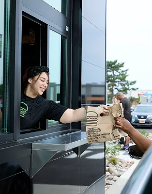 Shake Shack employee handing a customer their order through a drive-thru window