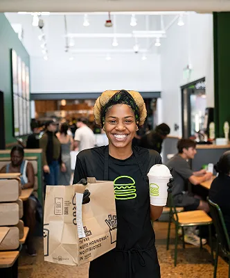 A smiling Shake Shack employee holding a Shake Shack bag and a drink