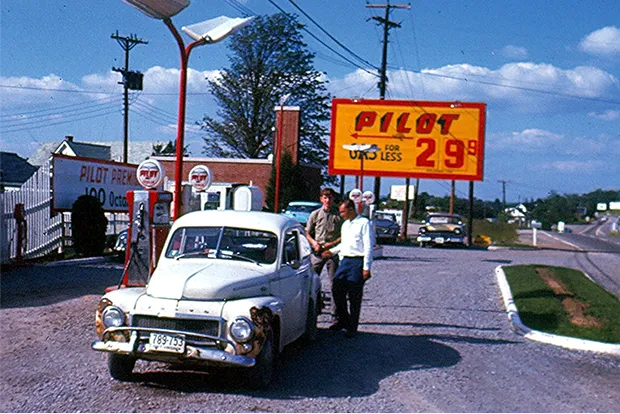 Vintage photo of an early Pilot gas station with attendants fueling a classic car beside a large sign advertising gas for 29 cents.