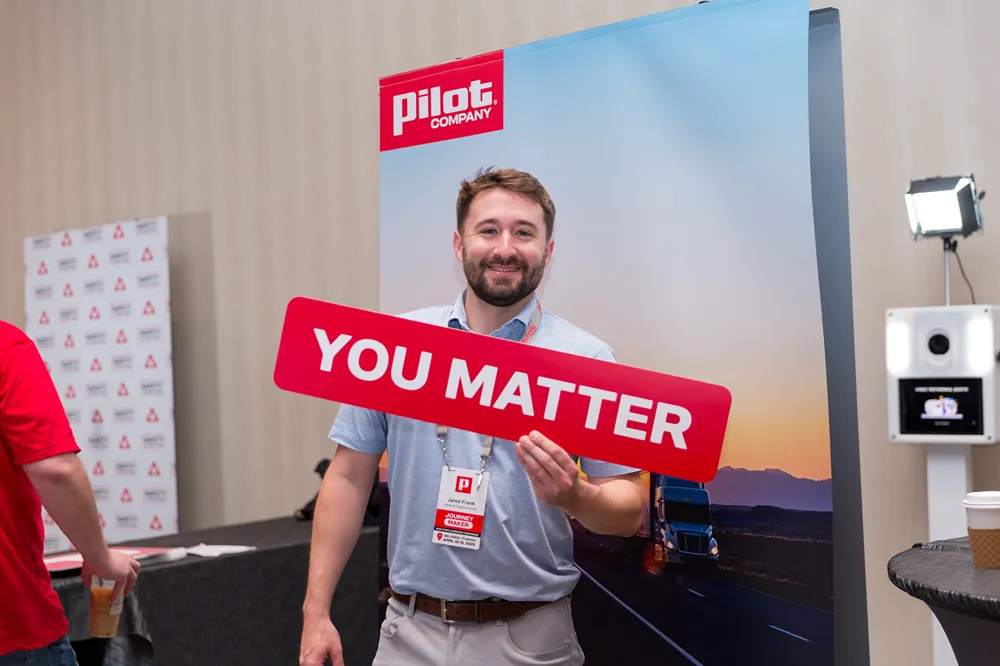 A smiling Pilot Company employee is holding a red sign that says 'YOU MATTER' at a corporate event.
