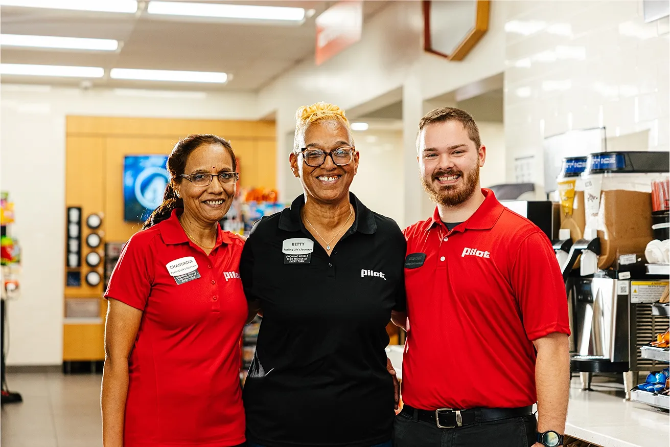Three diverse and smiling Pilot Flying J team members are posing together in a store.
