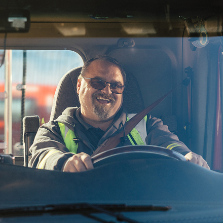 A cheerful truck driver is smiling while sitting in the driver's seat of his truck.