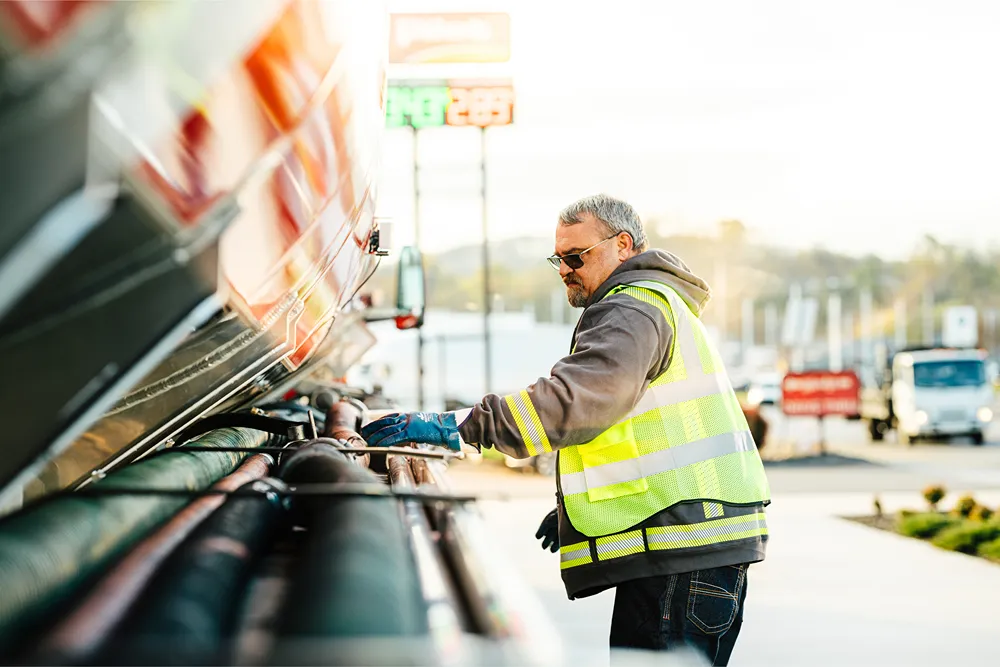 A driver or technician is working on a fuel tanker truck at a truck stop.