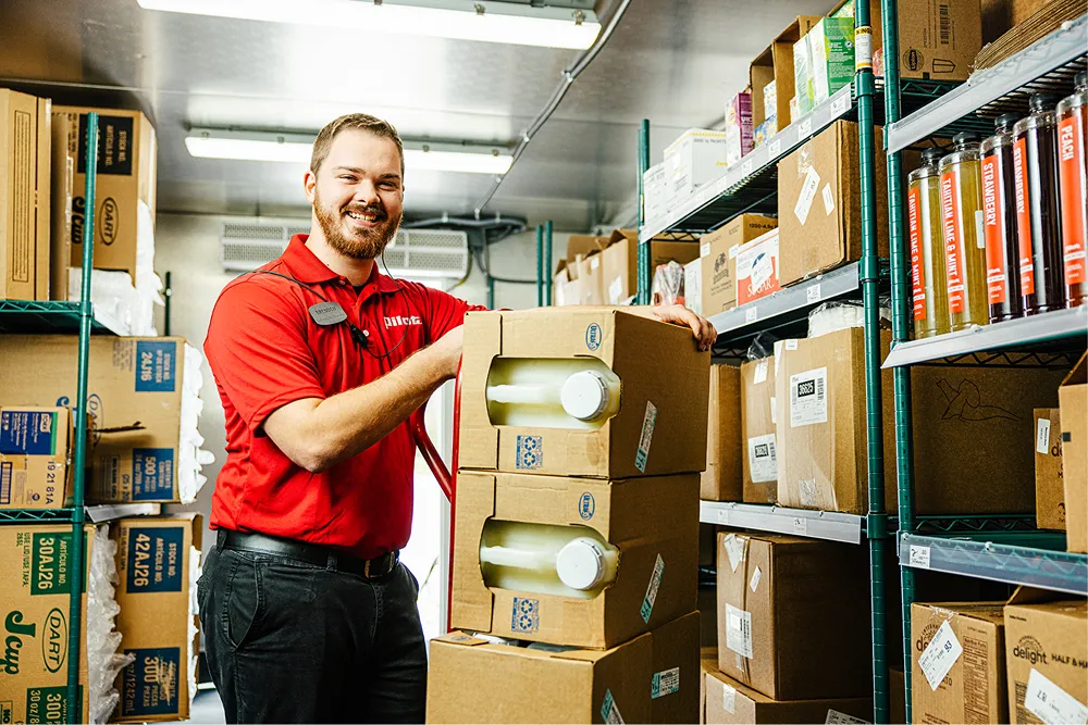 A smiling Pilot Flying J team member is proudly standing next to boxes in a stockroom.
