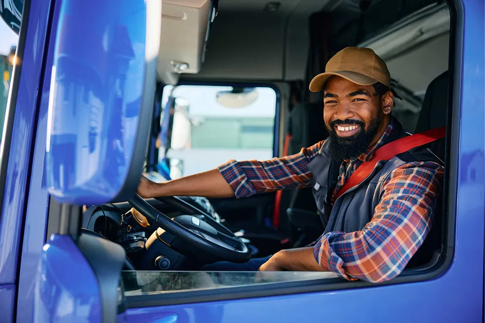A happy truck driver is smiling from the cab of his blue semi-truck.