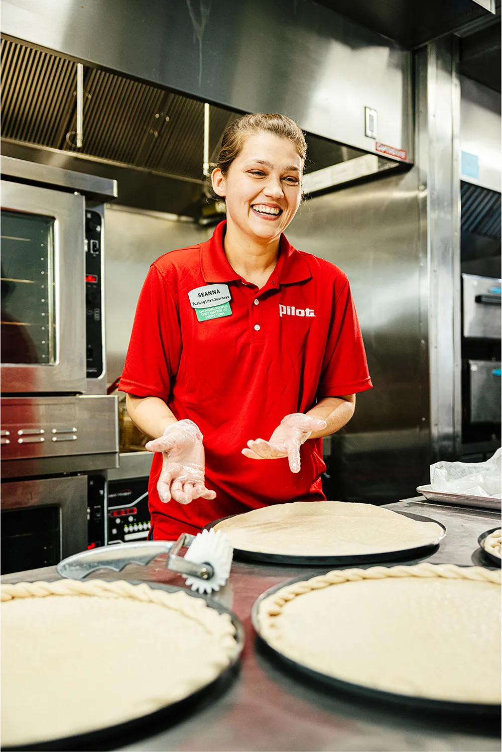 A smiling Pilot Flying J team member is preparing pizza dough in a commercial kitchen.