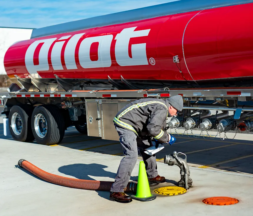 A fuel tanker driver is carefully connecting a hose to the tanker trailer for loading or unloading.