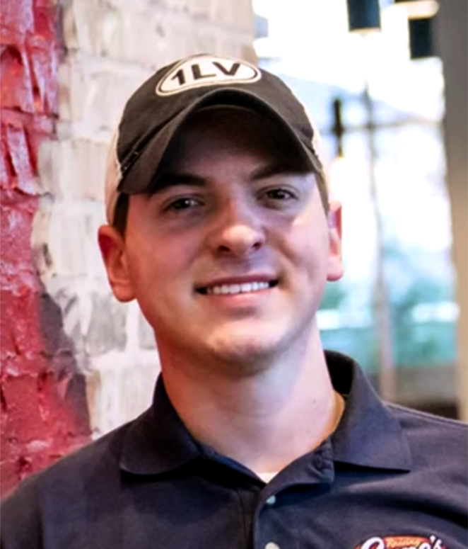 a man wearing a hat standing next to a brick wall
