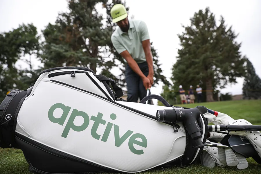 a man playing golf, beside a bag with Aptive logo on it