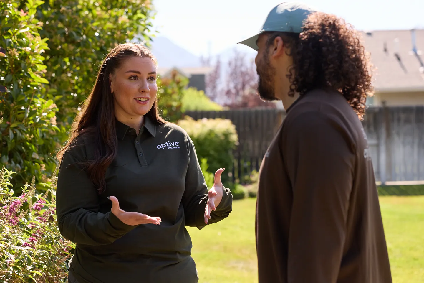 Two Aptive Environmental employees in uniform, a woman gesturing while speaking to a man outdoors