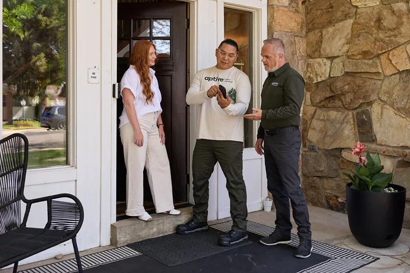 Two Aptive Environmental employees speaking with a female homeowner at her front door