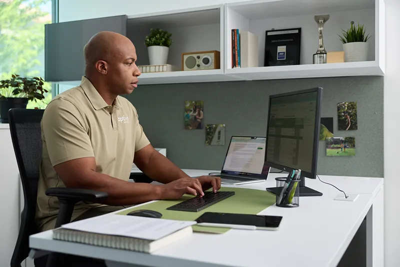 A male Aptive Environmental employee working at a computer in a modern office cubicle