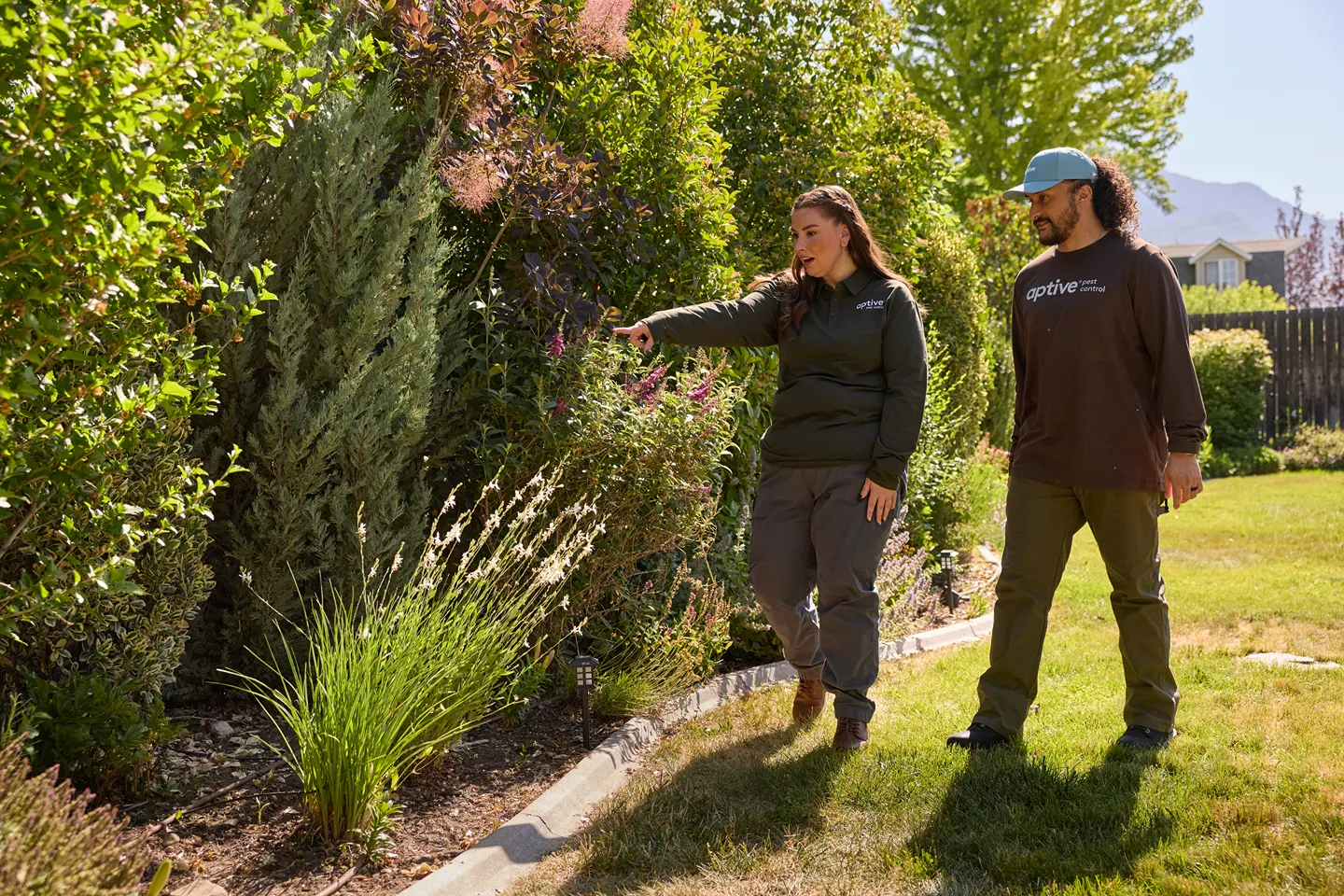 An Aptive Environmental employee points out something in a garden to a male colleague, both in uniform