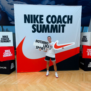 一位年輕女子站在一塊巨大的背景板前微笑，手中拿著一個巨大的紅色耐吉標誌剪紙和一個白色標誌。