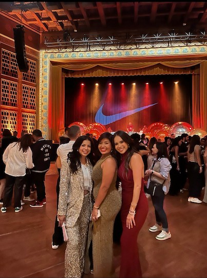 三位身著禮服和晚禮服的女士在裝飾華麗的劇院參加活動時微笑合影。