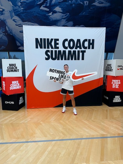 一位年輕女子站在一塊巨大的背景板前微笑，手中拿著一個巨大的紅色耐吉標誌剪紙和一個白色標誌。