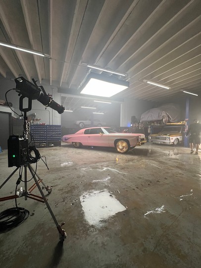 鏡頭切換到拍攝現場，展現了一間光線昏暗的車庫，裡面停著一輛經典的粉紅色低底盤車，配有金色輪圈。