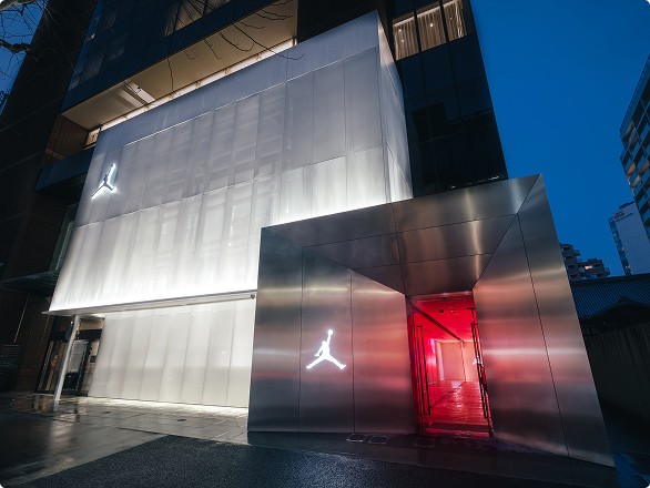 A modern building with a metallic facade and a red-lit entrance, featuring a white jumping silhouette logo