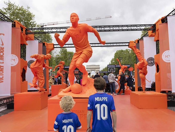 Outdoor exhibit with large orange statues of a soccer player and two children