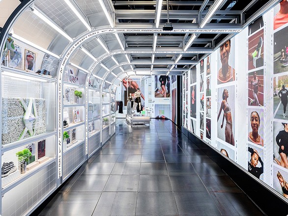 A modern corridor with display shelves and large photographs on the walls, illuminated by overhead fluorescent lights