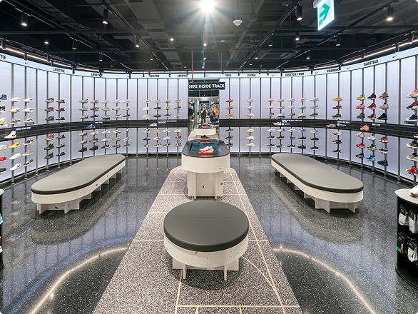 Interior of a shoe store with curved shelving displaying various shoes, arranged around a central area with benches