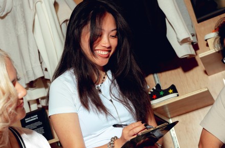 Three people smiling and discussing in a clothing store, holding a clipboard