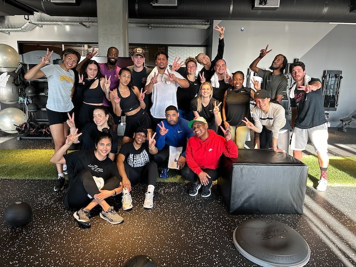 Un groupe de personnes posant dans une salle de sport, portant des vêtements de sport et faisant des signes de paix