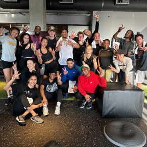 Un groupe de personnes posant dans une salle de sport, portant des vêtements de sport et faisant des signes de paix