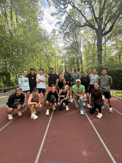 Un groupe de seize personnes sur une piste de course rouge, entourée de verdure et de grands arbres par une journée ensoleillée