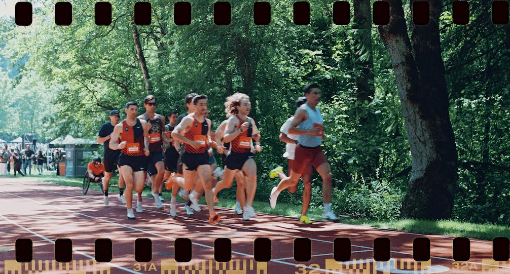 Un groupe de coureurs sur une piste rouge entourée d'arbres verts, avec une bordure de bande de film