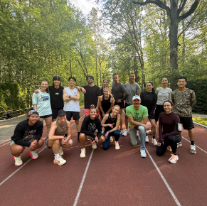 Un groupe de seize personnes sur une piste de course rouge, entourée de verdure et de grands arbres par une journée ensoleillée