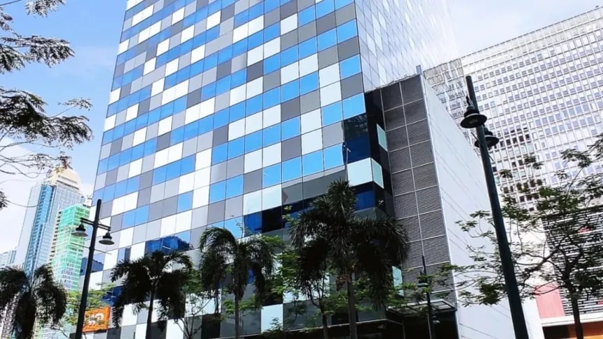 A modern high-rise building with a facade of blue, white, and gray glass panels, surrounded by palm trees and streetlights, set against a cityscape with other tall buildings.