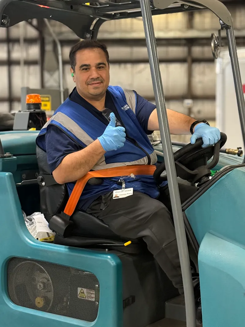 A dedicated KBS crew member operating a floor cleaning machine in a large facility.