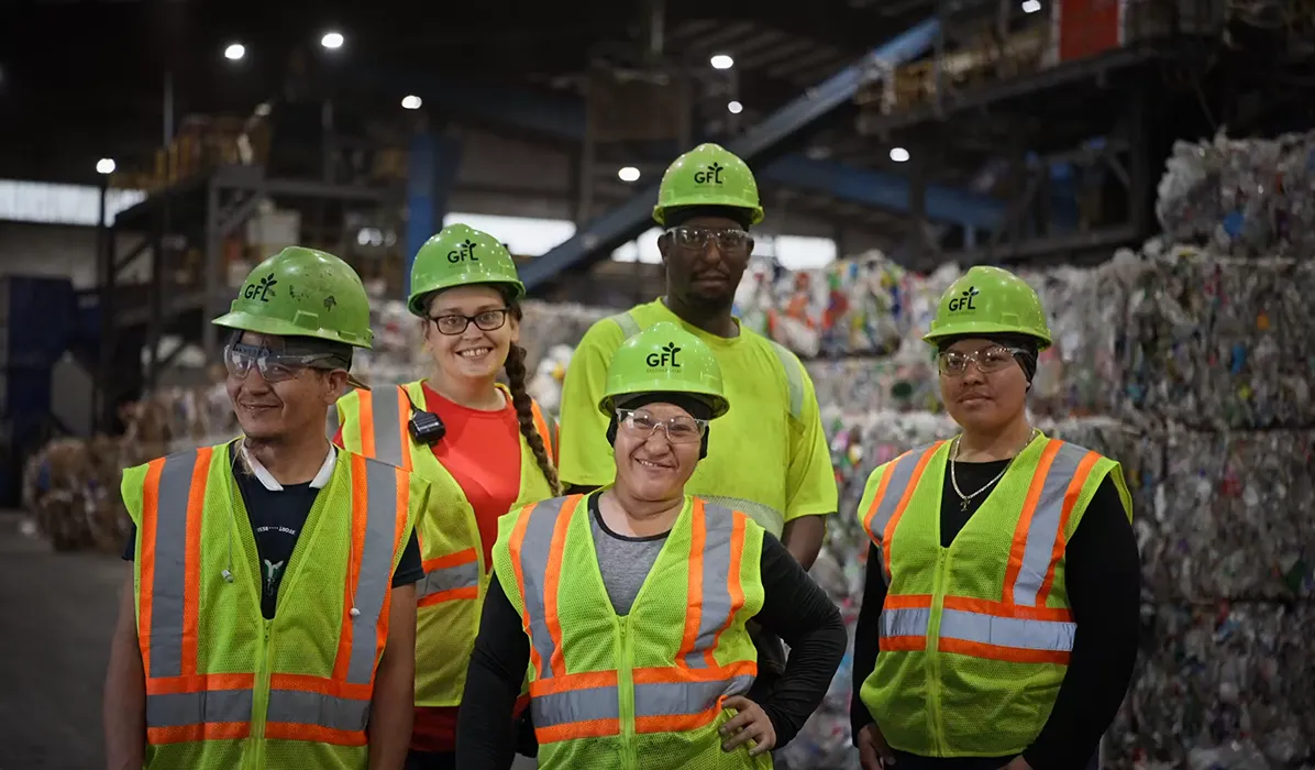 Team of field workers in safety vests and helmets at a recycling plant