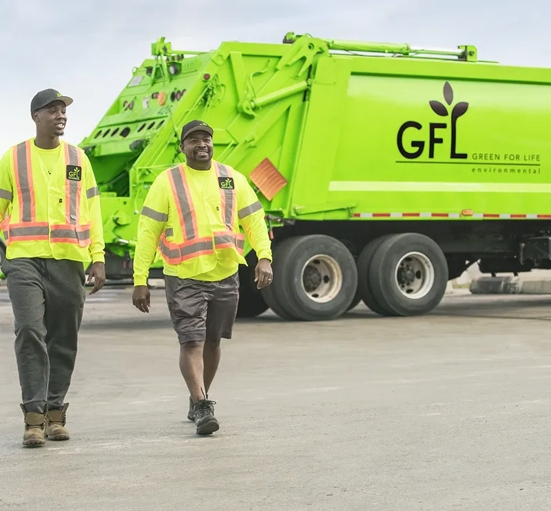 Deux éboueurs en uniformes vert vif s'éloignent d'un camion poubelle vert lime.