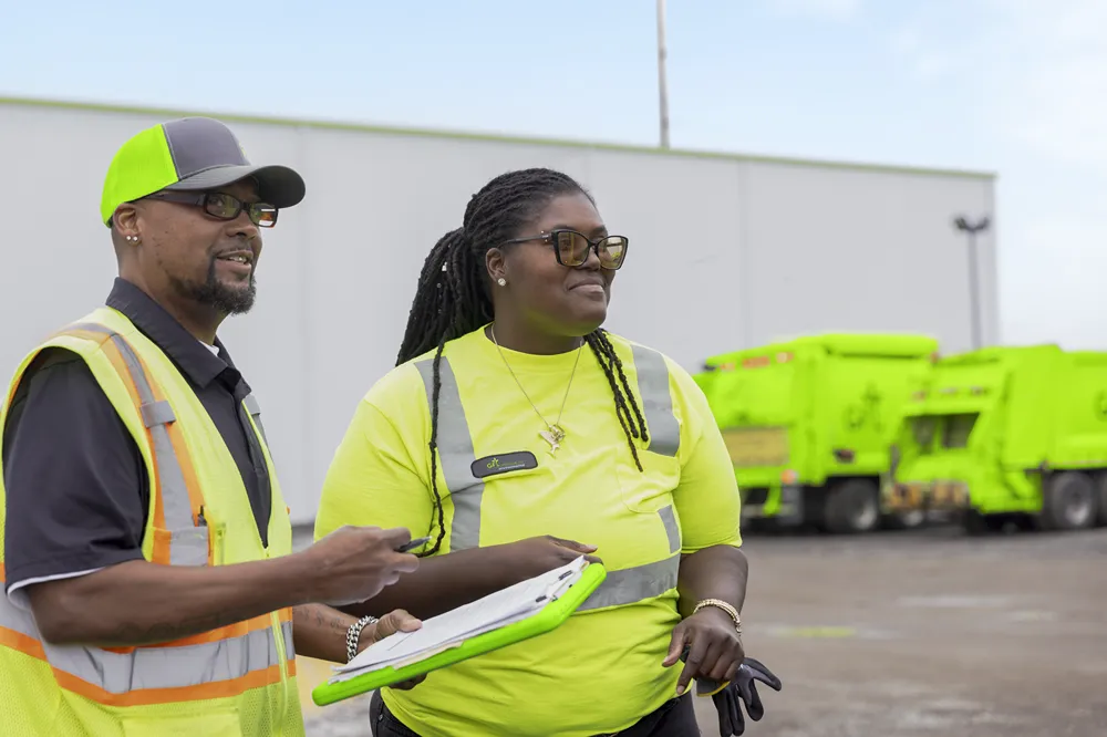 Deux éboueurs portant des gilets de sécurité jaune vif examinent des documents.