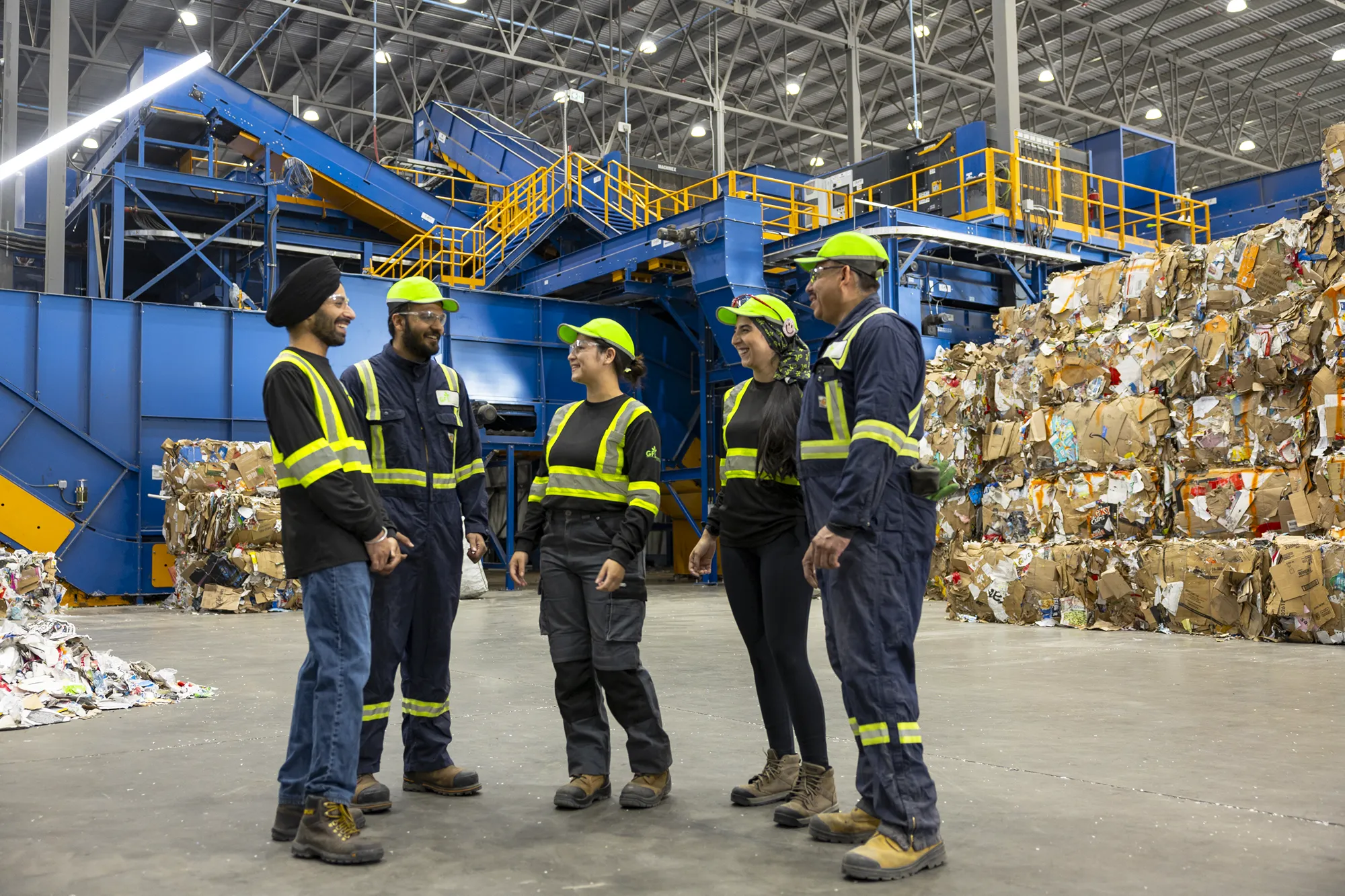 Four people in safety gear smiling and talking at a recycling plant hiring event